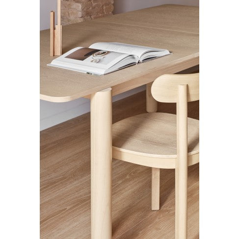 Wooden dining table with an open book on top, accompanied by a chair.